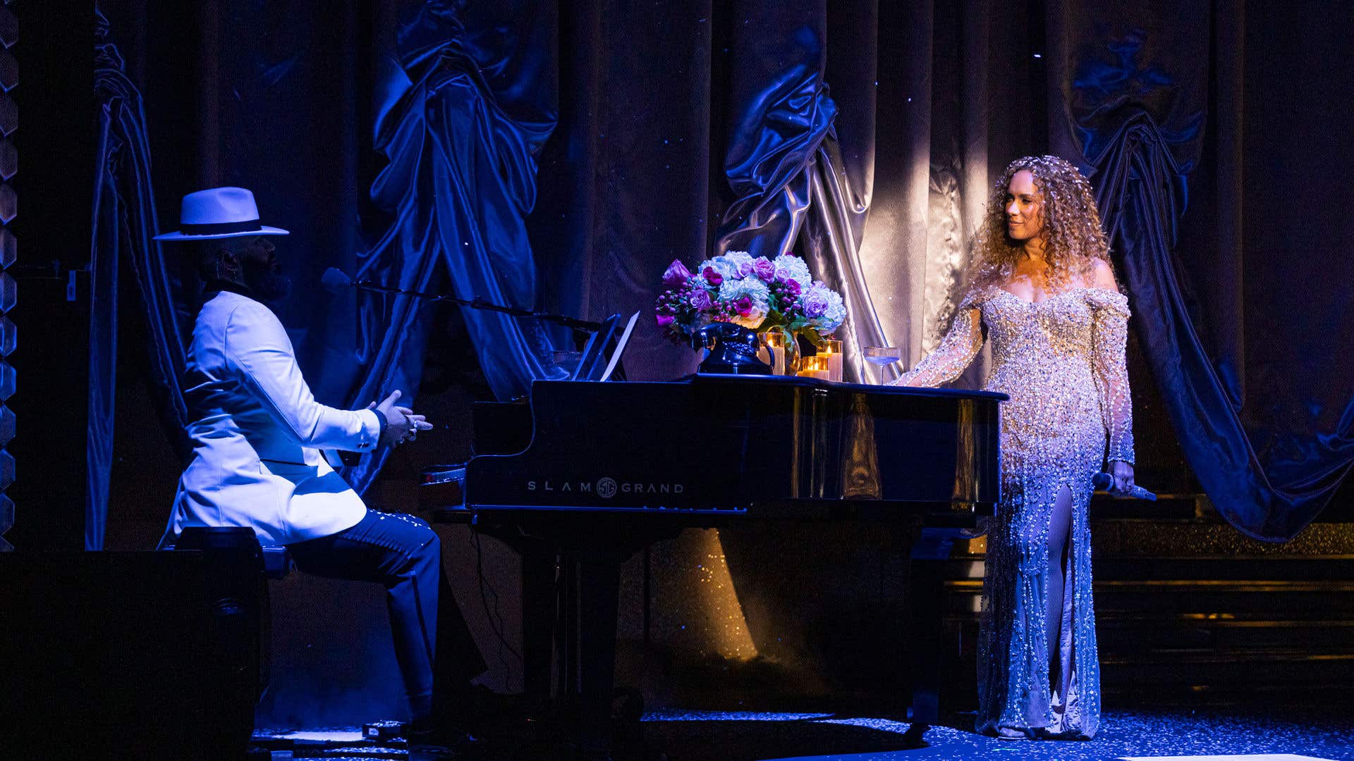 Leona Lewis in sparkling gown staring at a man in white hat and jacket playing the piano.