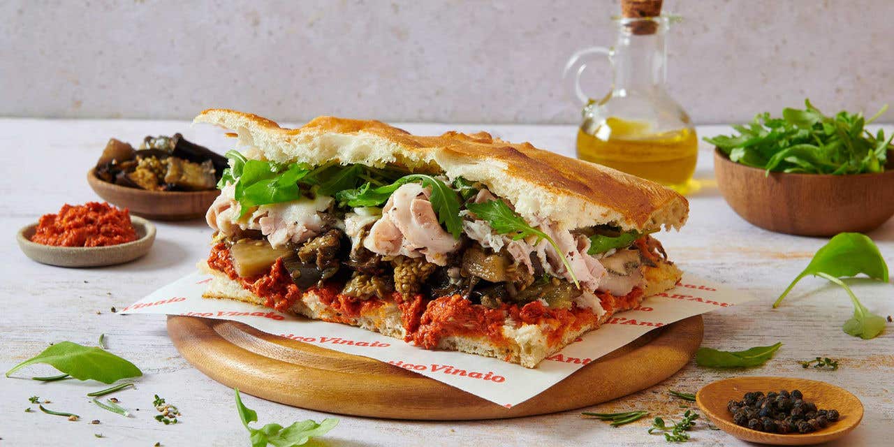 Large sandwich with turkey, lettuce, peppers and sun-dried tomatoes displayed on a table.