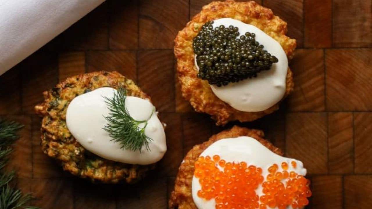 Three latkes topped with sour cream and each one with a different topping, crab, zucchini, and plain sour cream.
