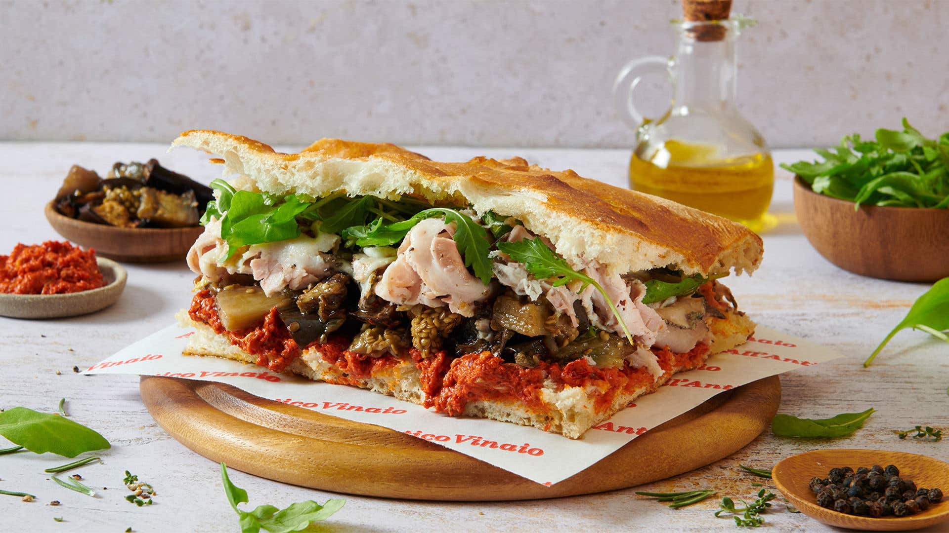 Large sandwich with turkey, lettuce, peppers and sun-dried tomatoes displayed on a table.